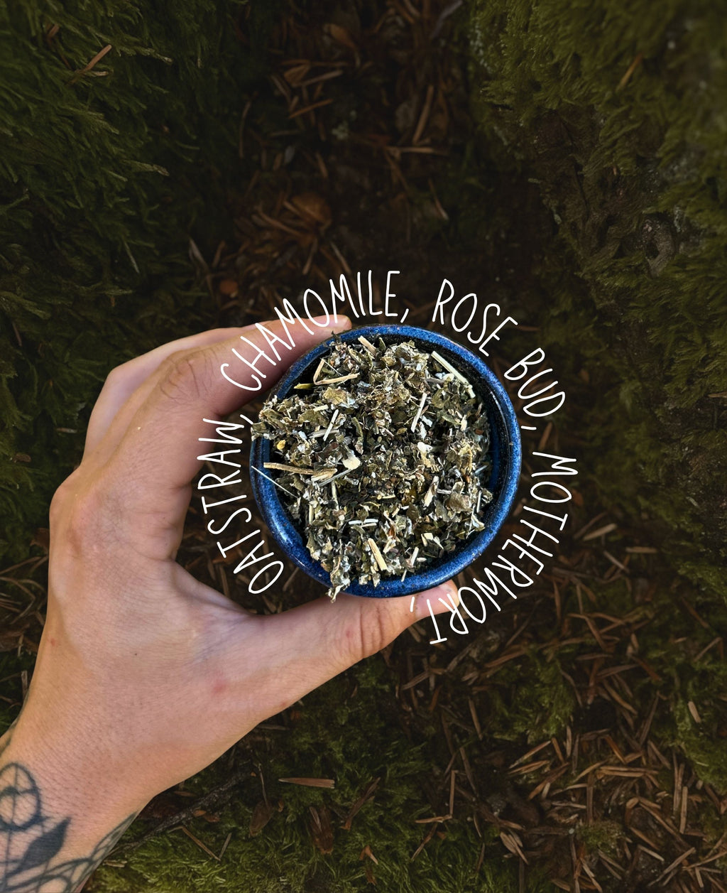 A hand holds a small blue bowl filled with dried herbs for a grief tea chamomile, rose bud, oatstraw, and motherwort against a dark green mossy forest background. White handwritten text overlays the center of the image.